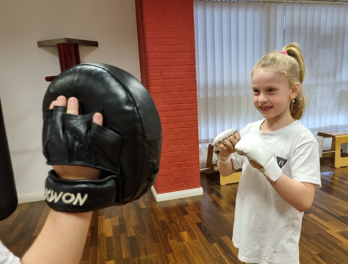 Mädchen mit Boxhandschuhen trainiert Schlagtechnik mit Pratze in Kampfsportschule